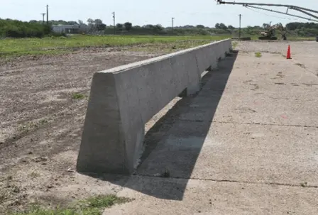 A concrete slotted median barrier separates a parking lot and field. 